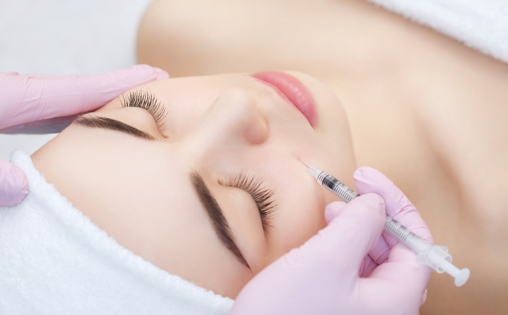 Woman receiving a cosmetic injection treatment, with a focus on facial enhancement. A professional in pink gloves administers the procedure, highlighting the growing trend of non-surgical beauty treatments.