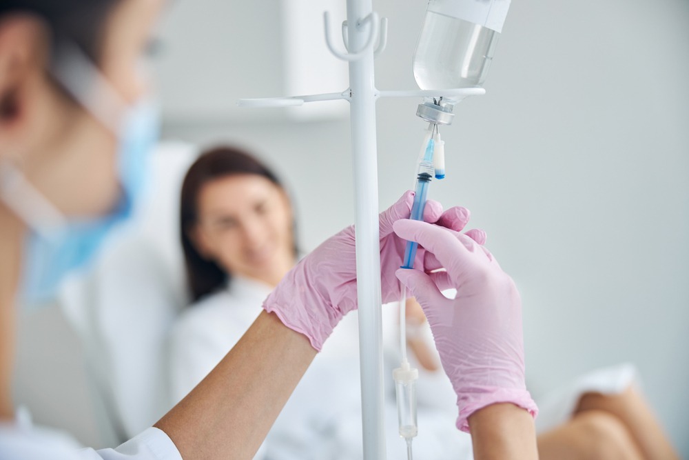Healthcare professional administering medication through an IV drip in a hospital setting, with a patient smiling in the background.