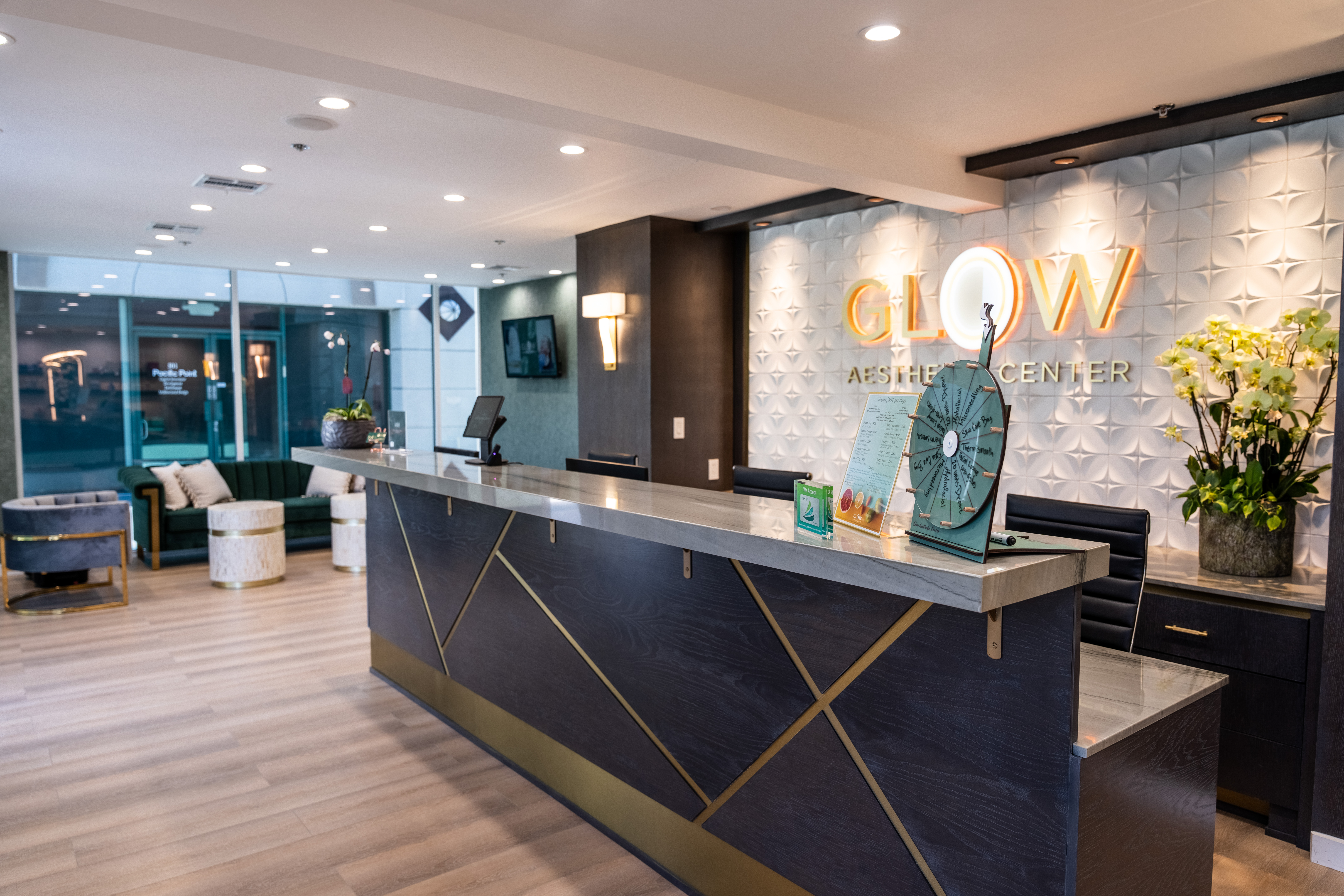 Modern reception area of Glow Aesthetic Center featuring a stylish front desk, decorative plants, and comfortable seating. The design includes elegant lighting and a textured wall with the center's name prominently displayed.